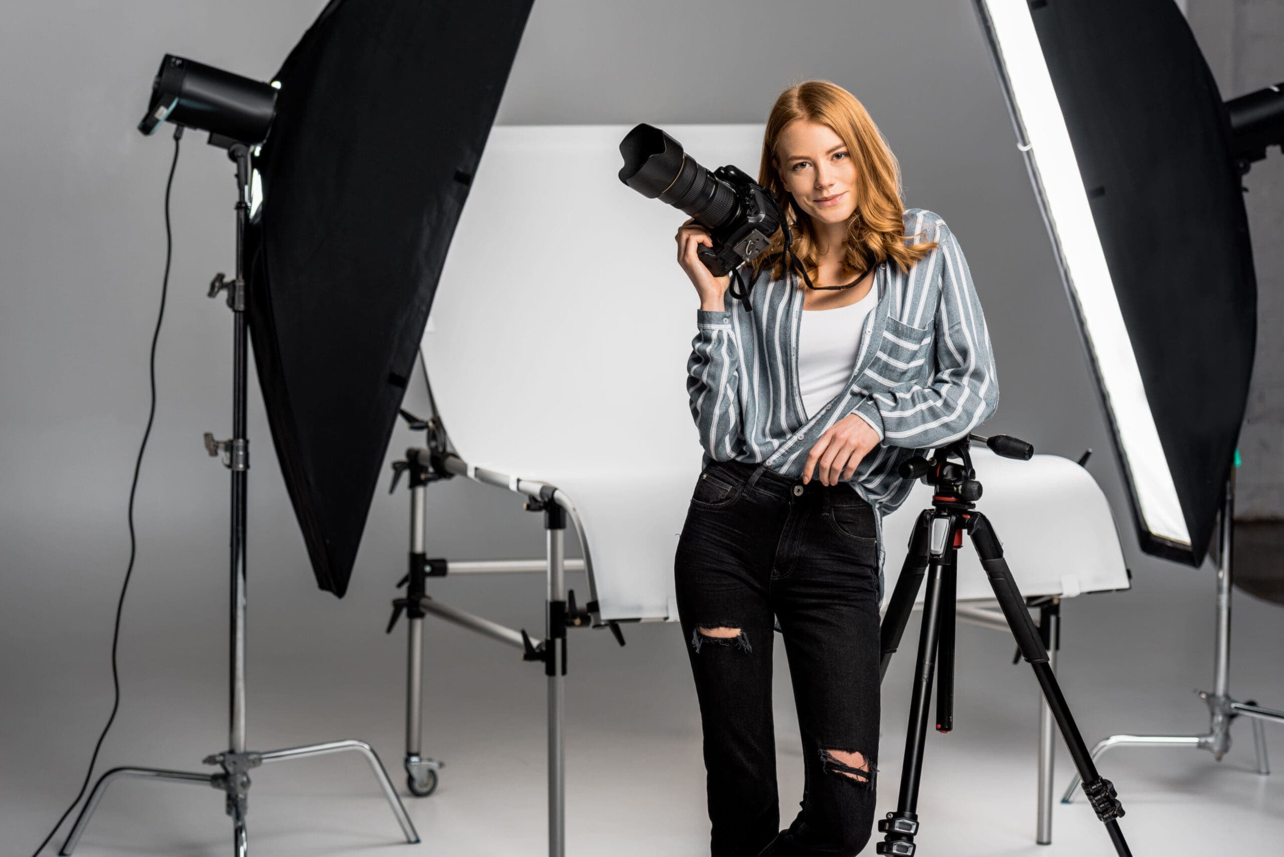 Photographer in a studio holding a camera, surrounded by softbox lighting and a tripod