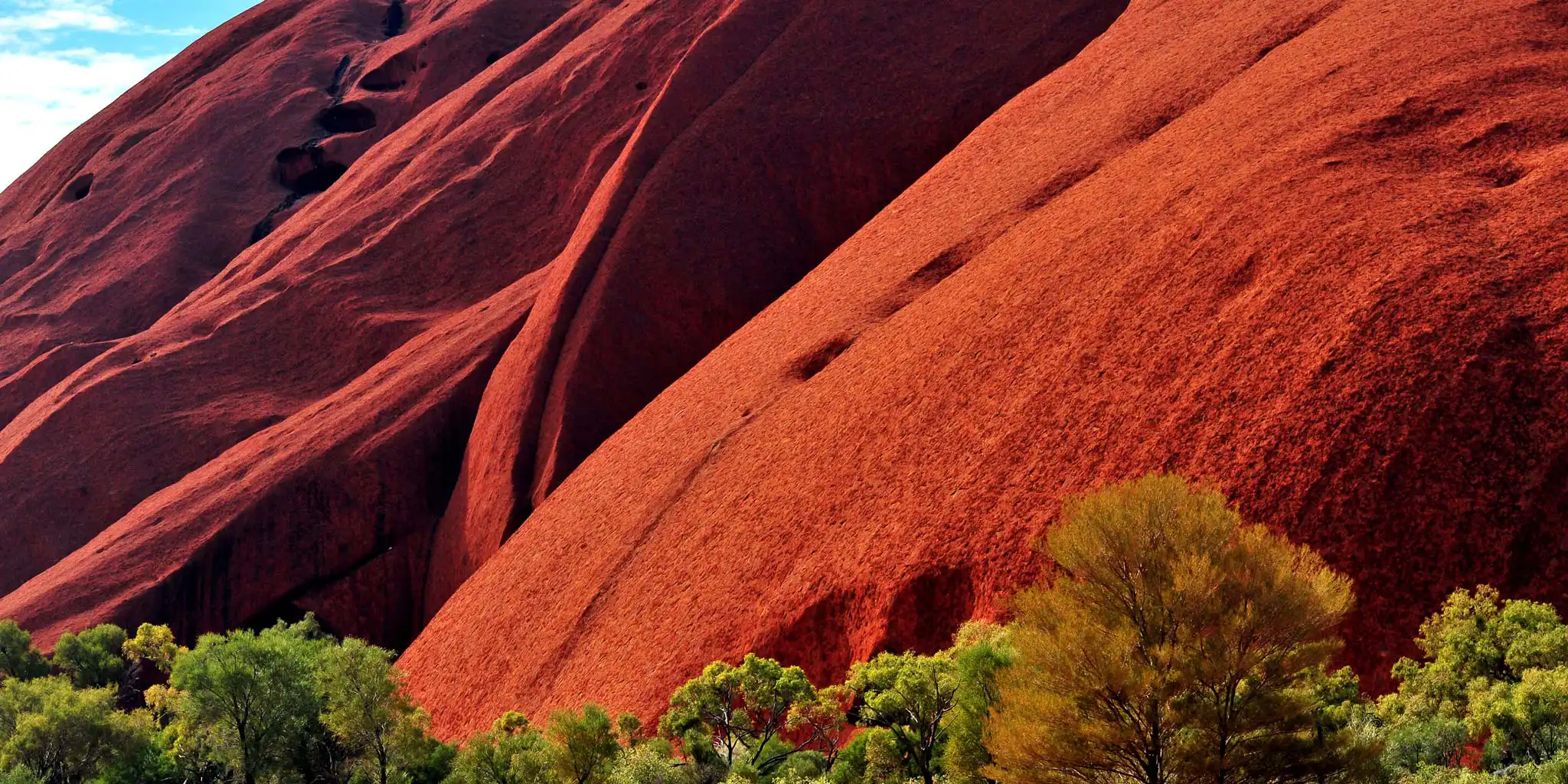Sunlit red rock formation with green trees in the foreground